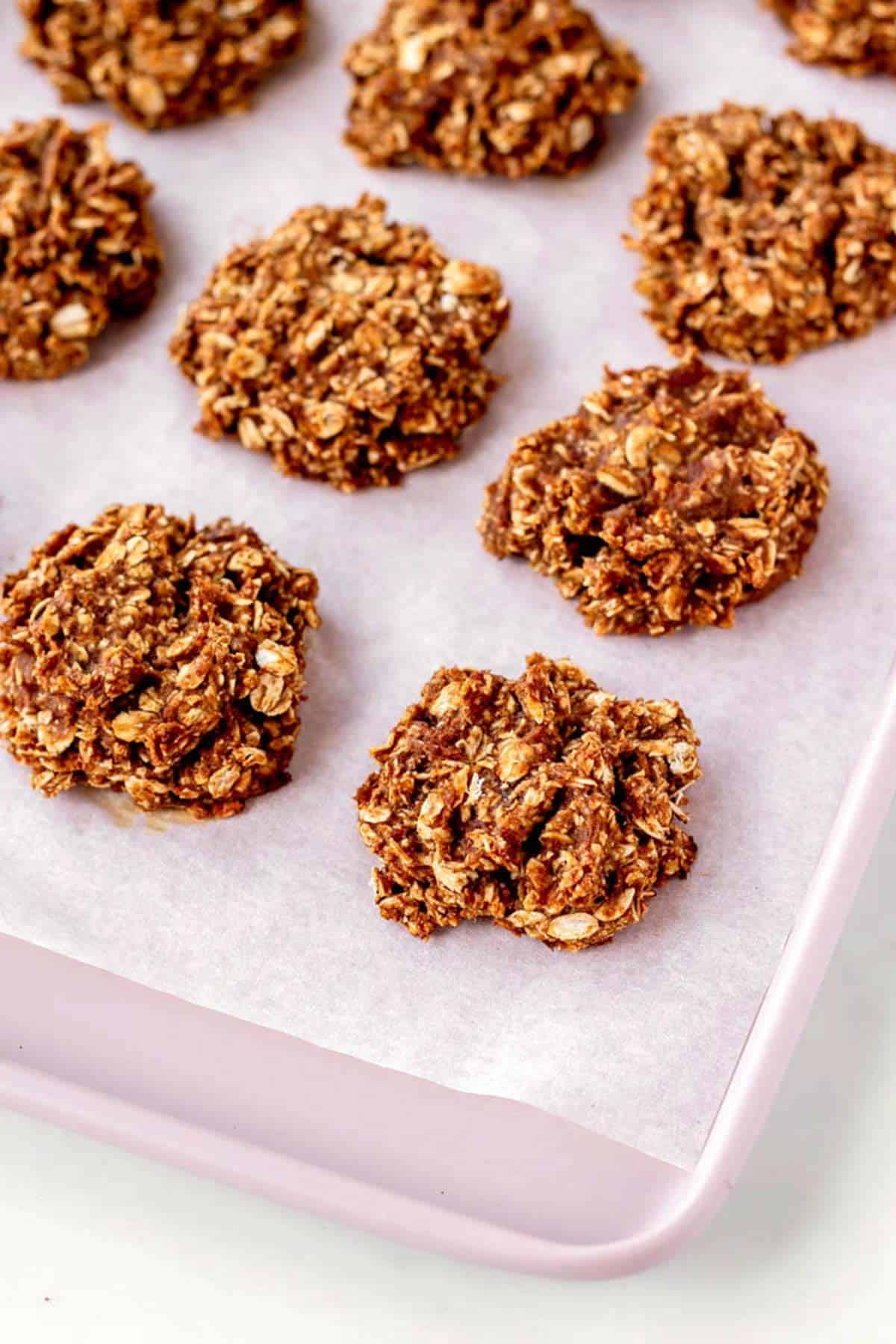 An up close image of the applesauce oatmeal cookies on a pink baking sheet.