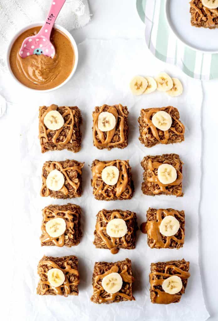 Twelve soft baked banana oatmeal bars topped with peanut butter and bananas.
