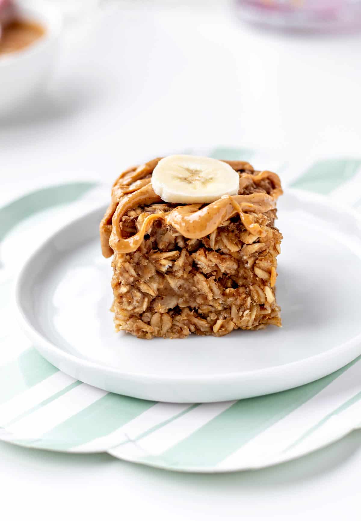 A 3-ingredient banana oatmeal bar on a small plate with a drizzle of peanut butter and banana slice.