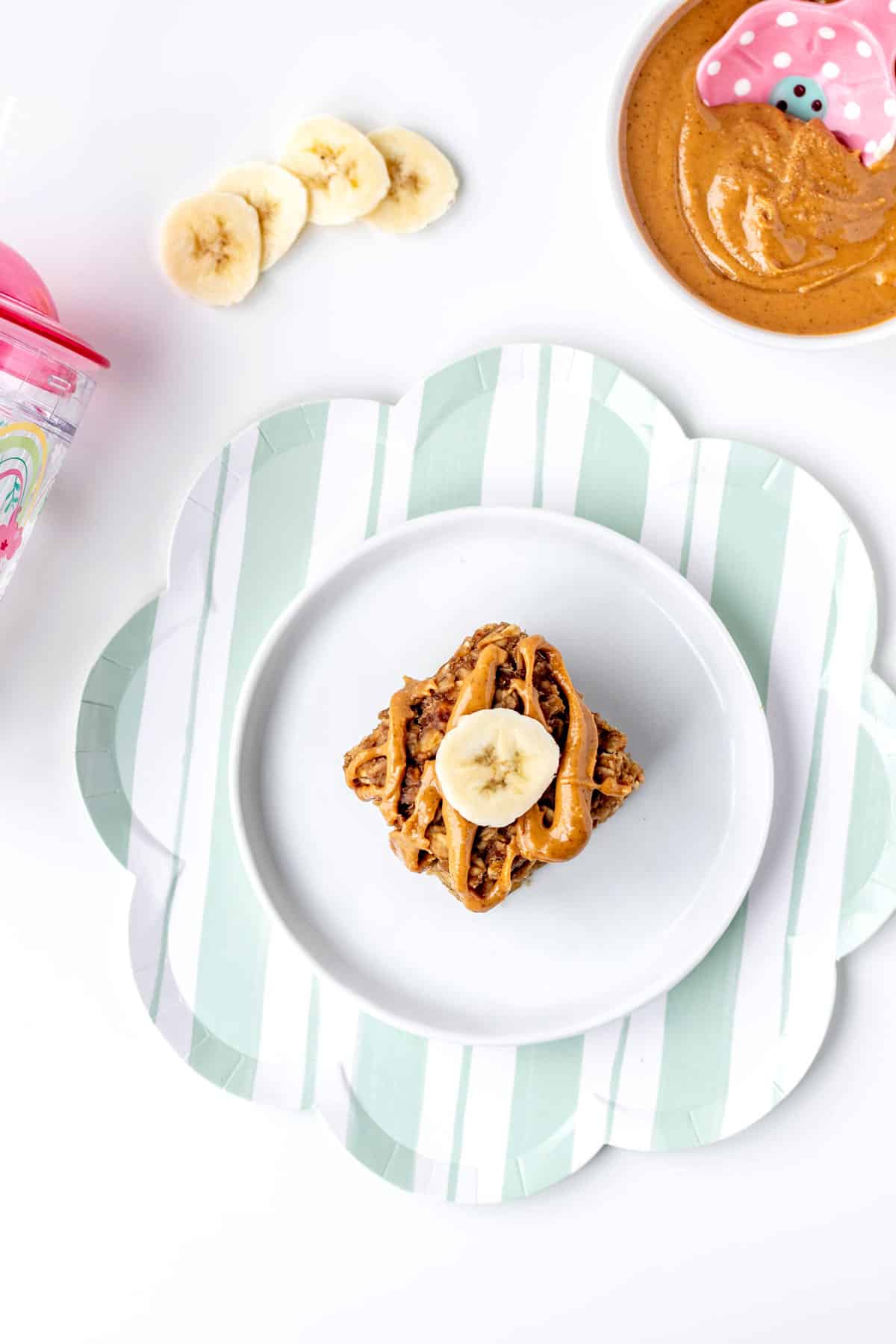 A peanut butter banana oatmeal bar on a plate with banana slices and peanut butter.