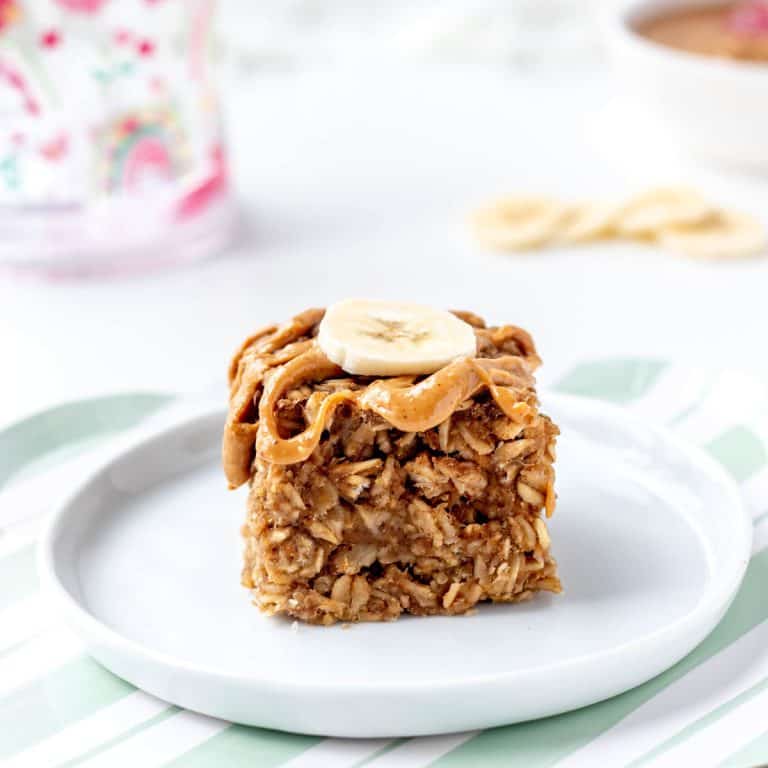A soft-baked banana oatmeal bar on a plate with peanut butter and banana on top.