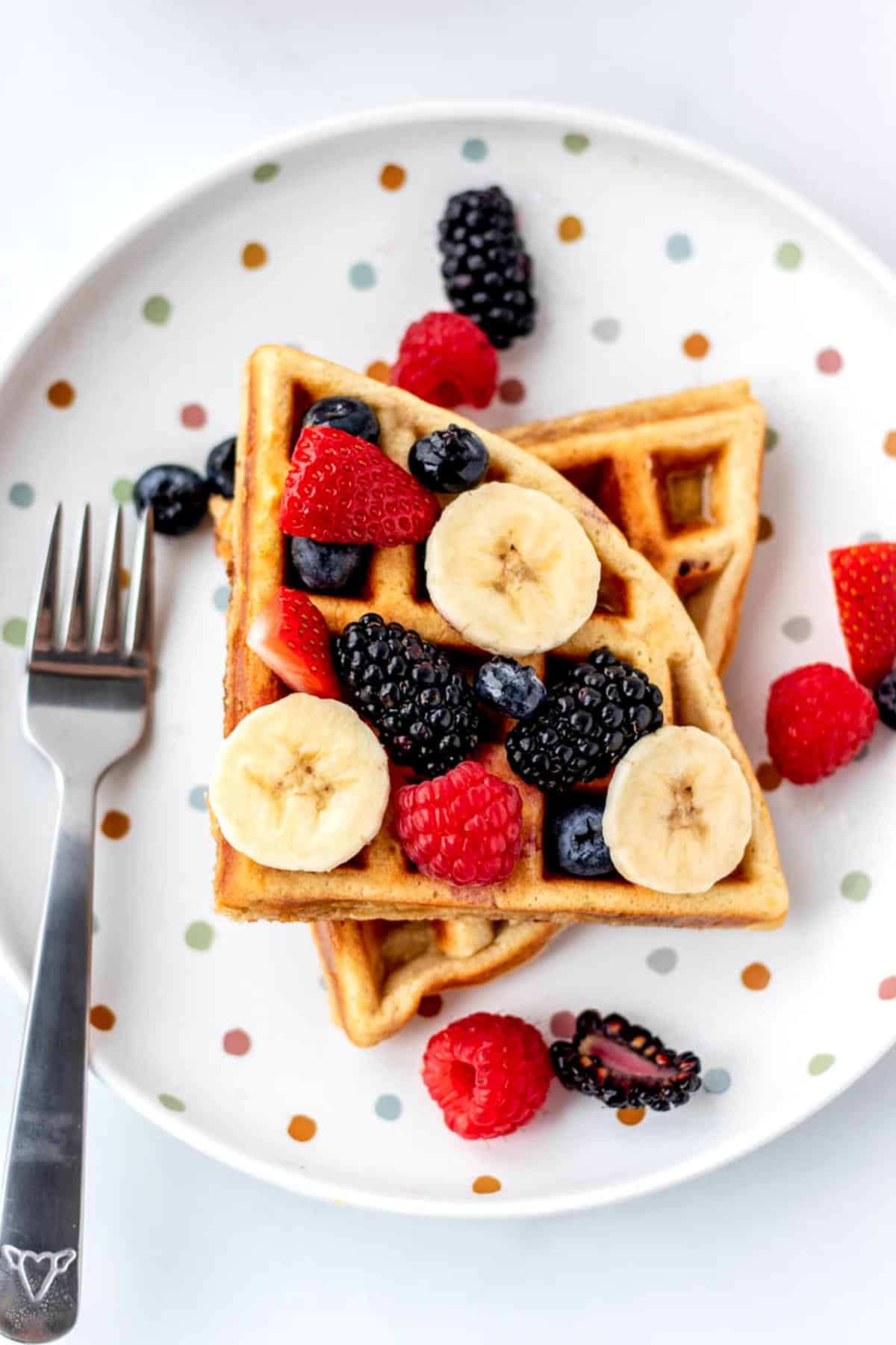 Overhead image of two 3-ingredient protein waffles on a plate topped with berries and banana.