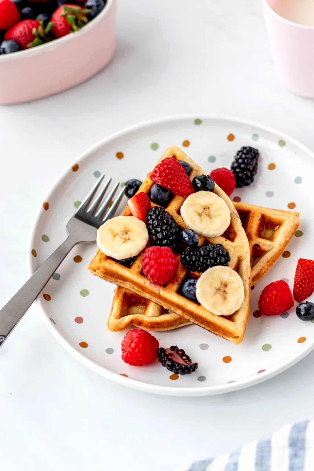 A fork next to two protein waffles on a plate topped with fruit. 