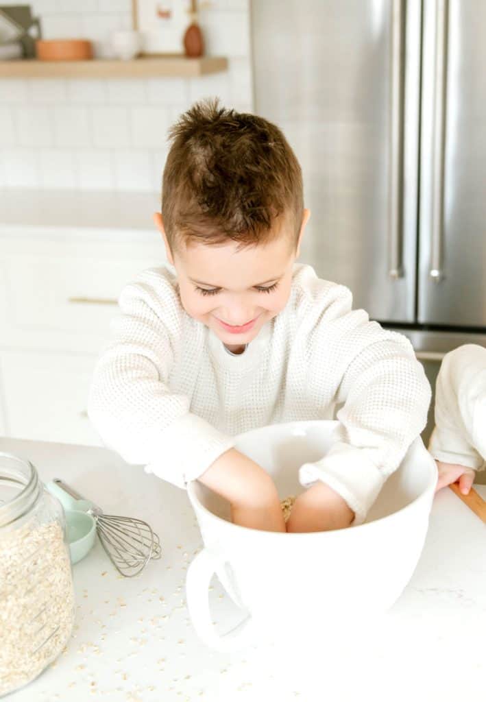 A little boy dipping his hands into a bowl of oats.