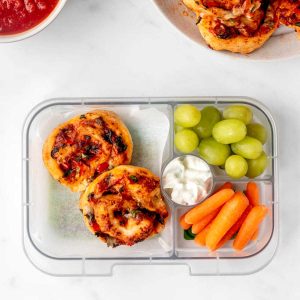 Air fryer pizza rolls in a lunch box with carrots, dip and grapes.