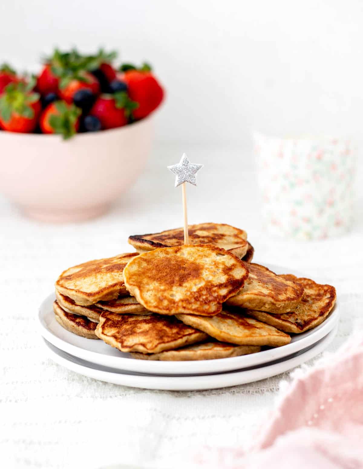 Baby oat pancakes on a two stacked white plates with a star pick poked into the middle.
