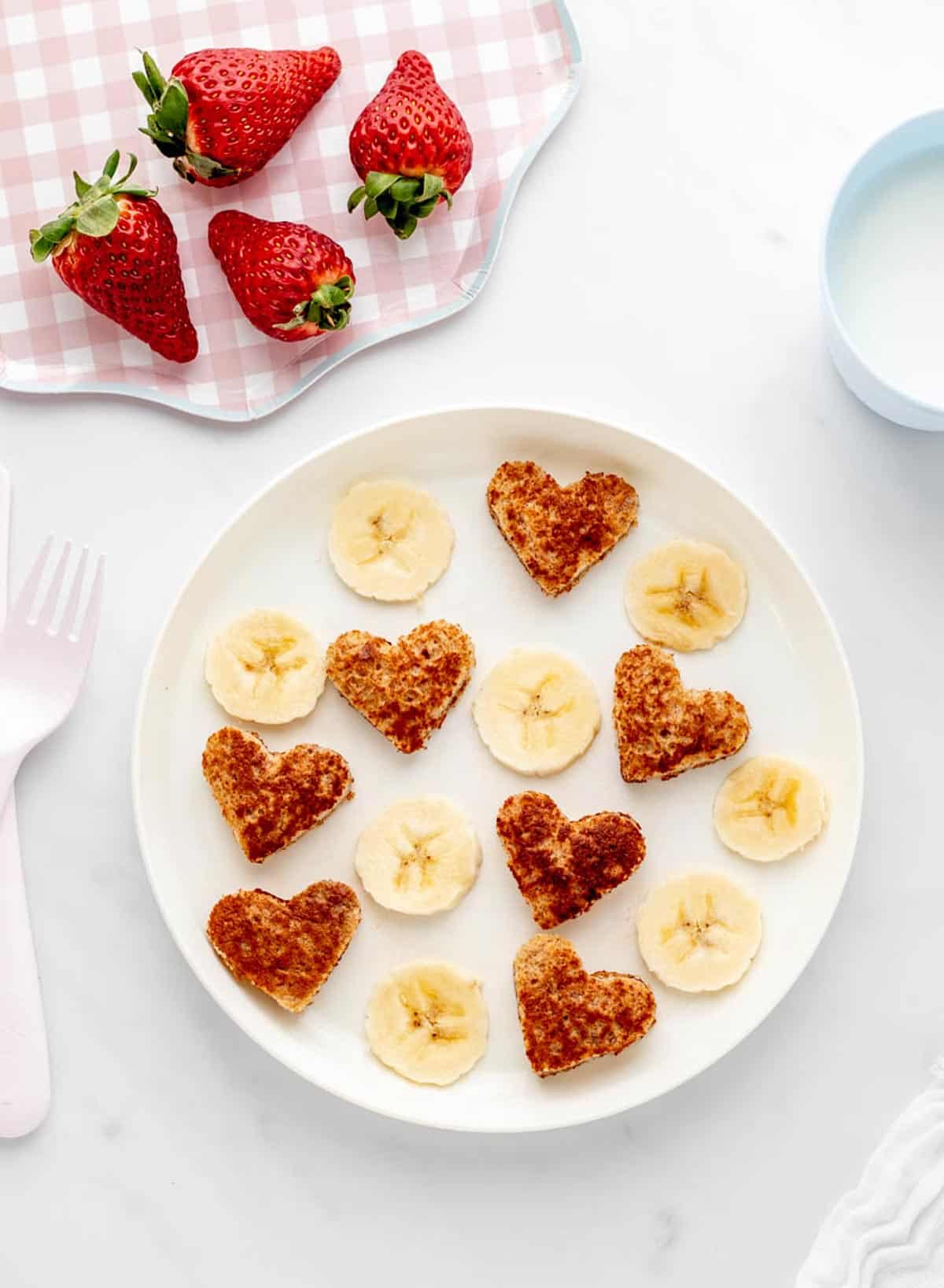 Banana French toast hearts on a white plate served with banana slices.