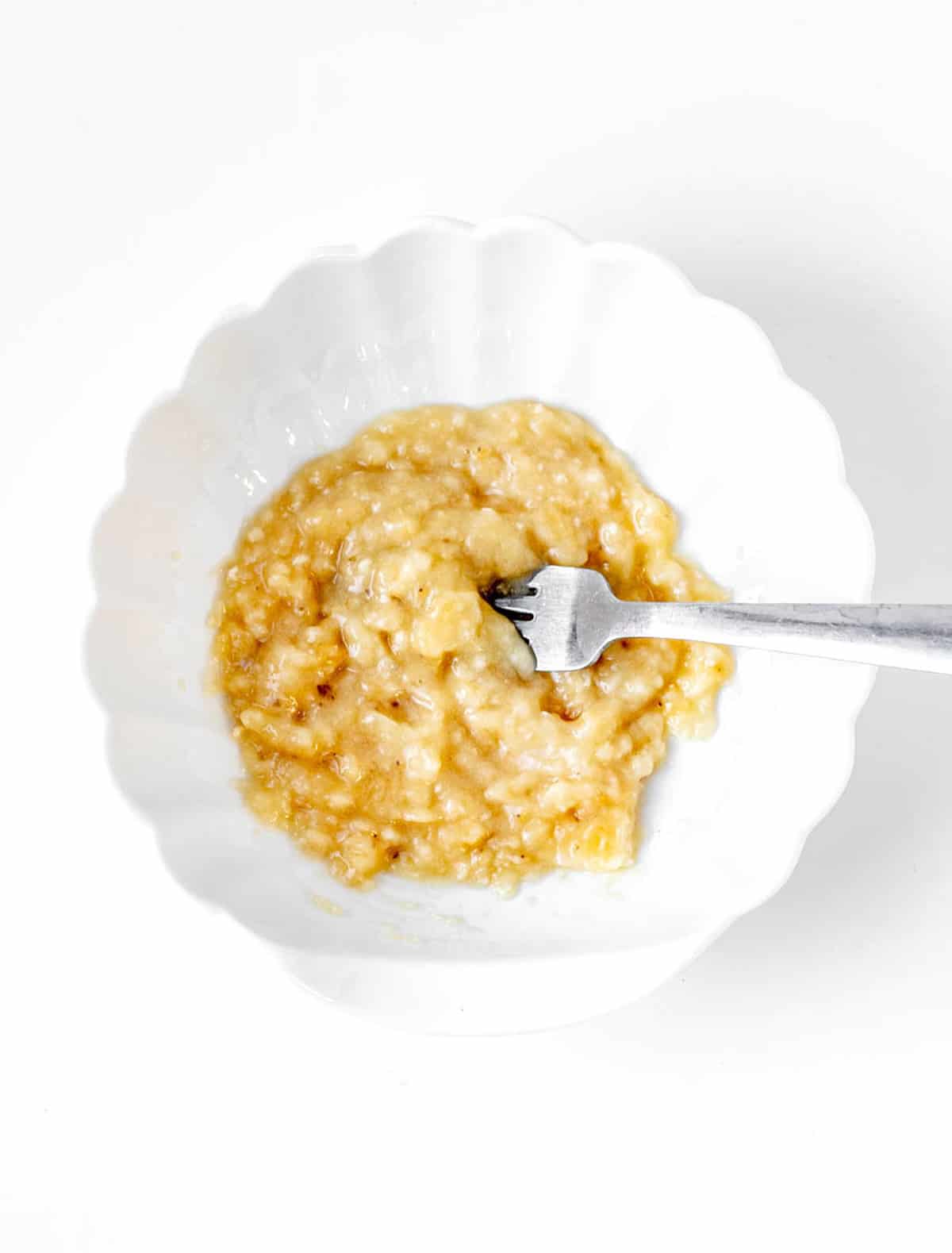 Mashed banana in a white bowl with a fork.