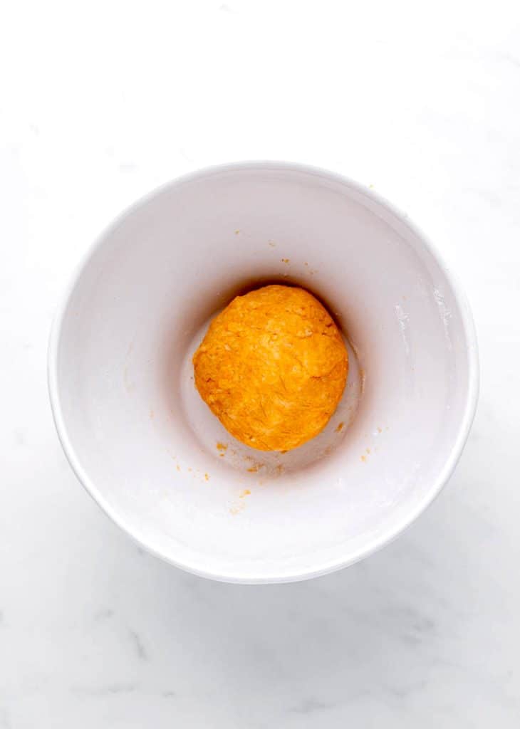 A ball of dough in a white bowl for the sweet potato cracker recipe.