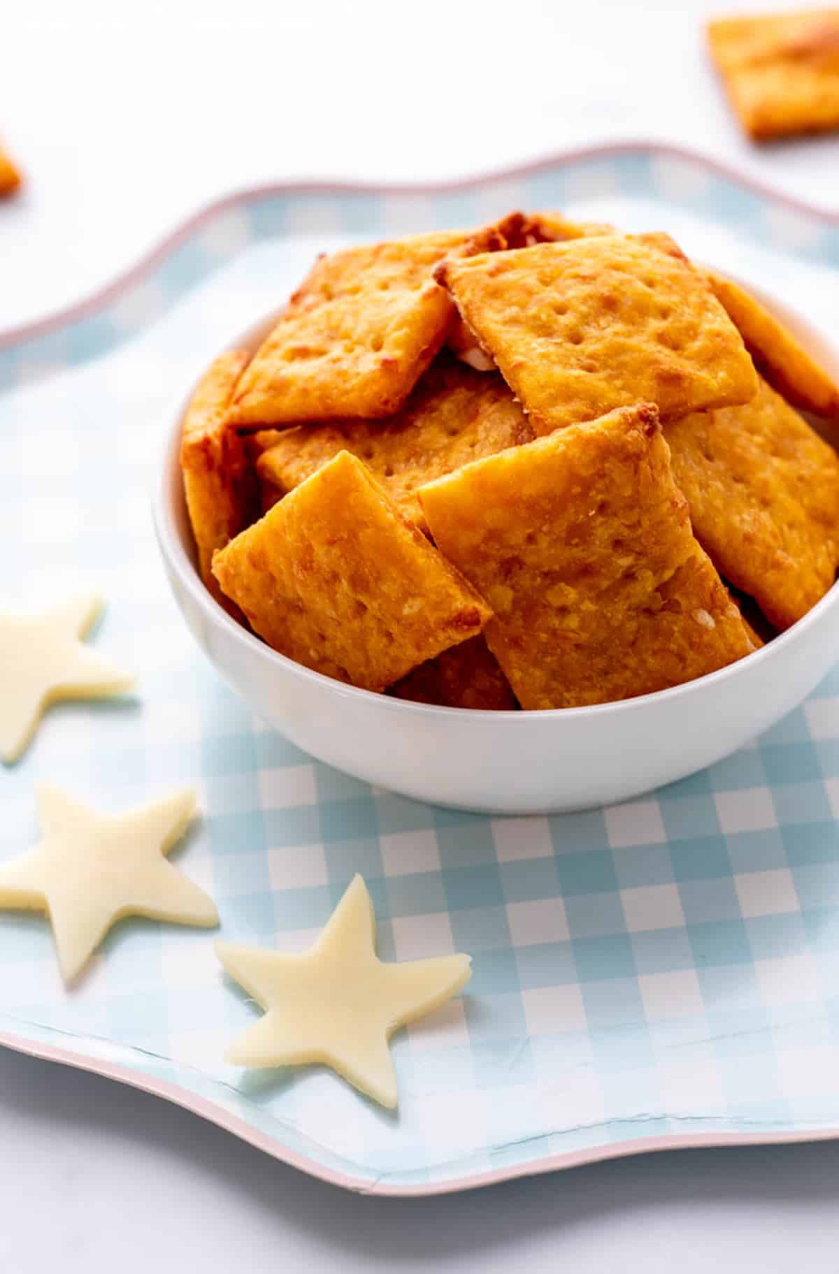 A bowl of homemade sweet potato crackers in a small white bowl next to star shaped cheese.