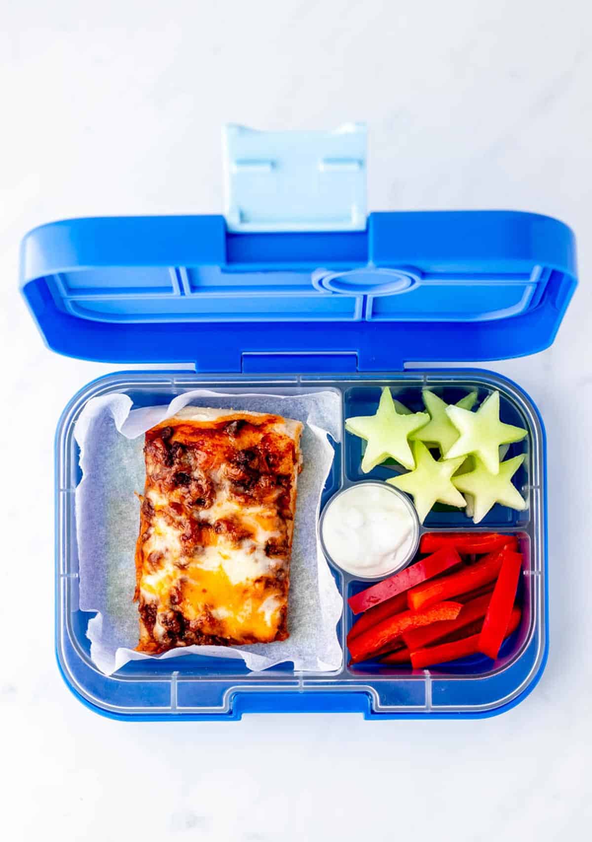 A slice of fiestada pizza in a blue lunch box with honey melon stars and red pepper strips.