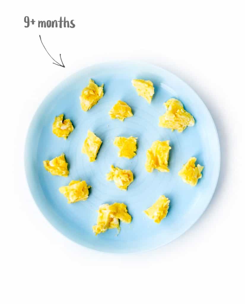 Scrambled eggs cut up for 9 month old baby on a blue plate.