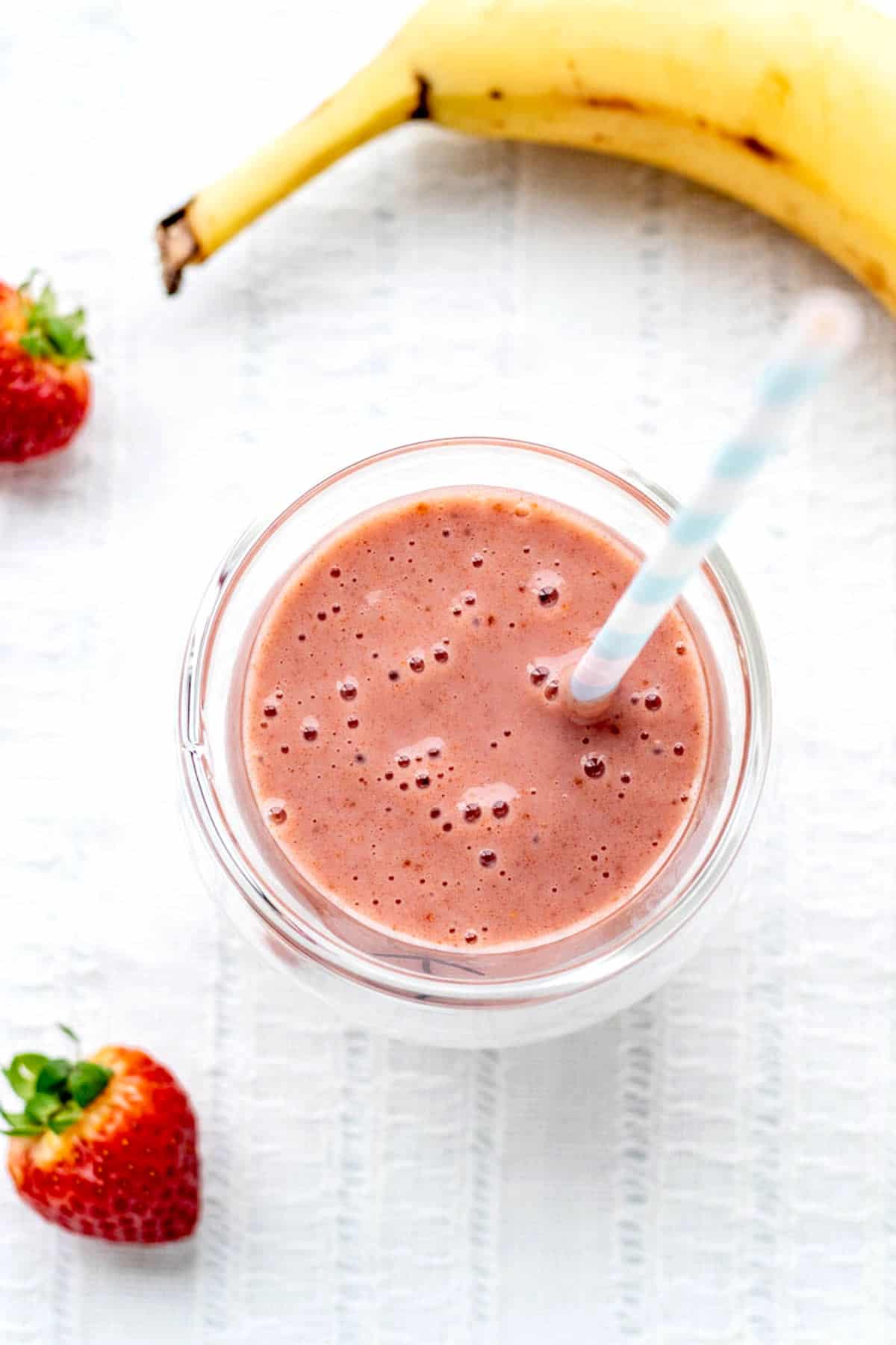 An overhead image of the strawberry banana smoothie in a glass with a straw next to a banana and strawberries.