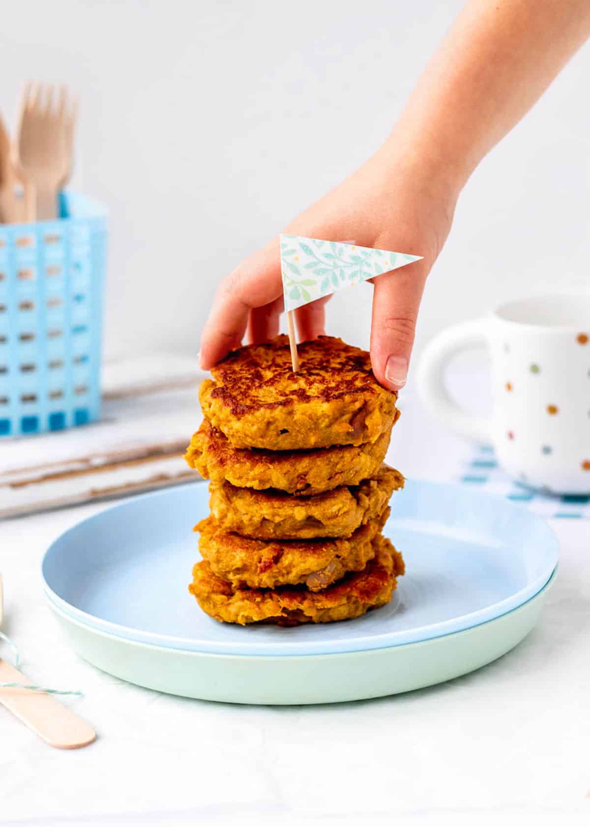 A child's hand picking up a sweet potato fritter off of a stack.