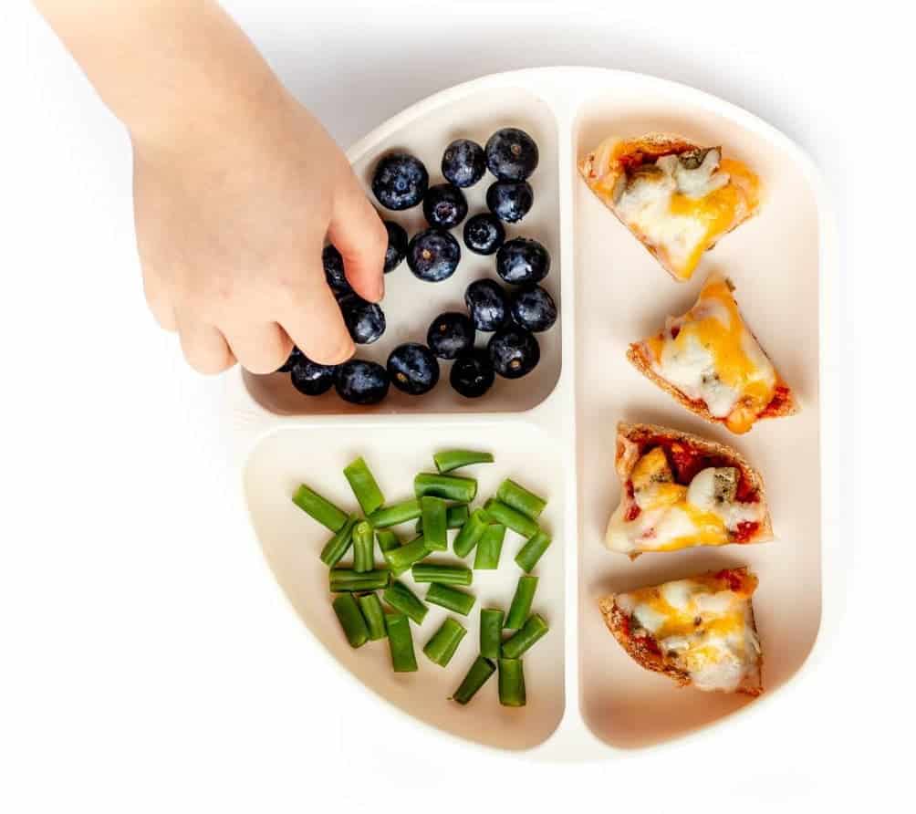 Childs hand reaching over plate with food.