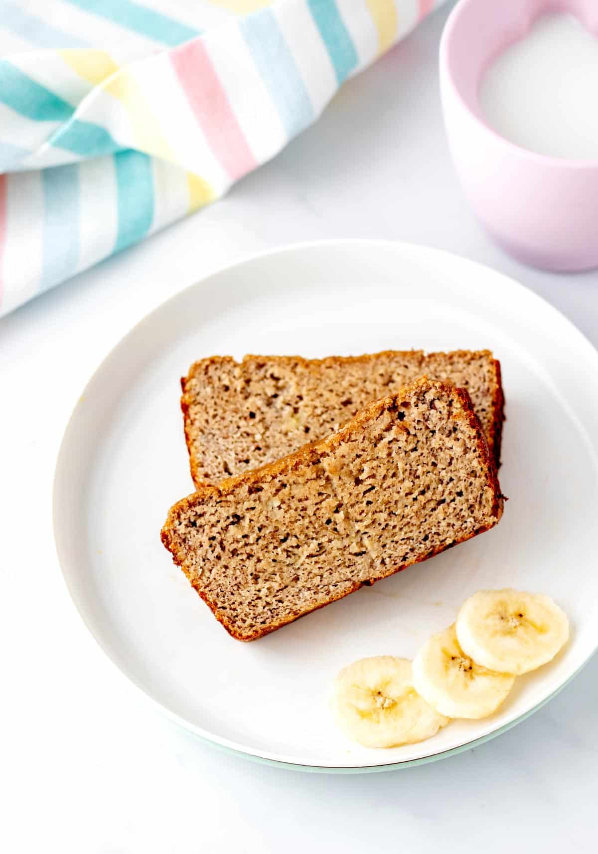 Two slices of no added sugar banana bread on a plate with banana slices.