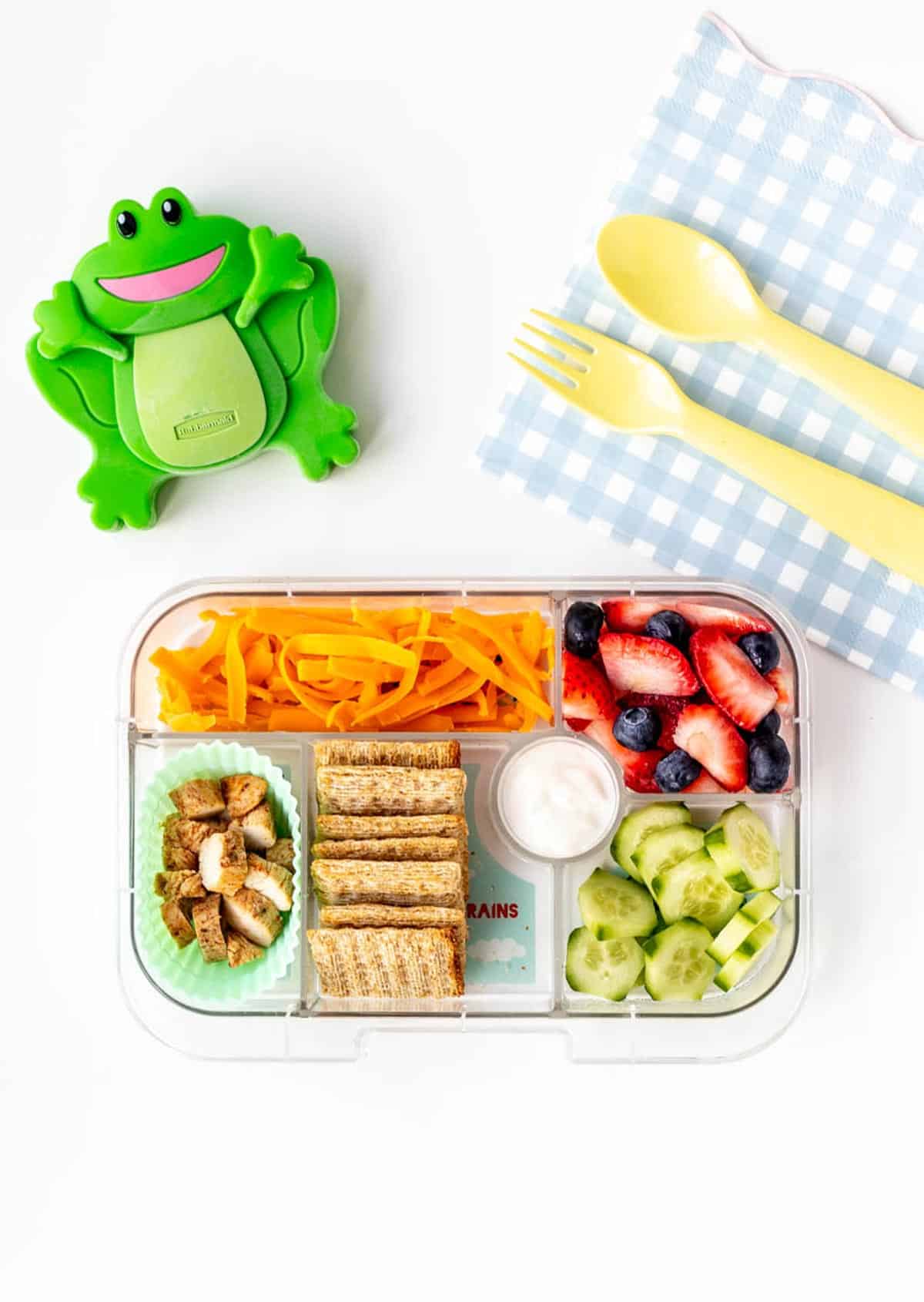 A bento lunch box with a frog shaped ice pack next to it.