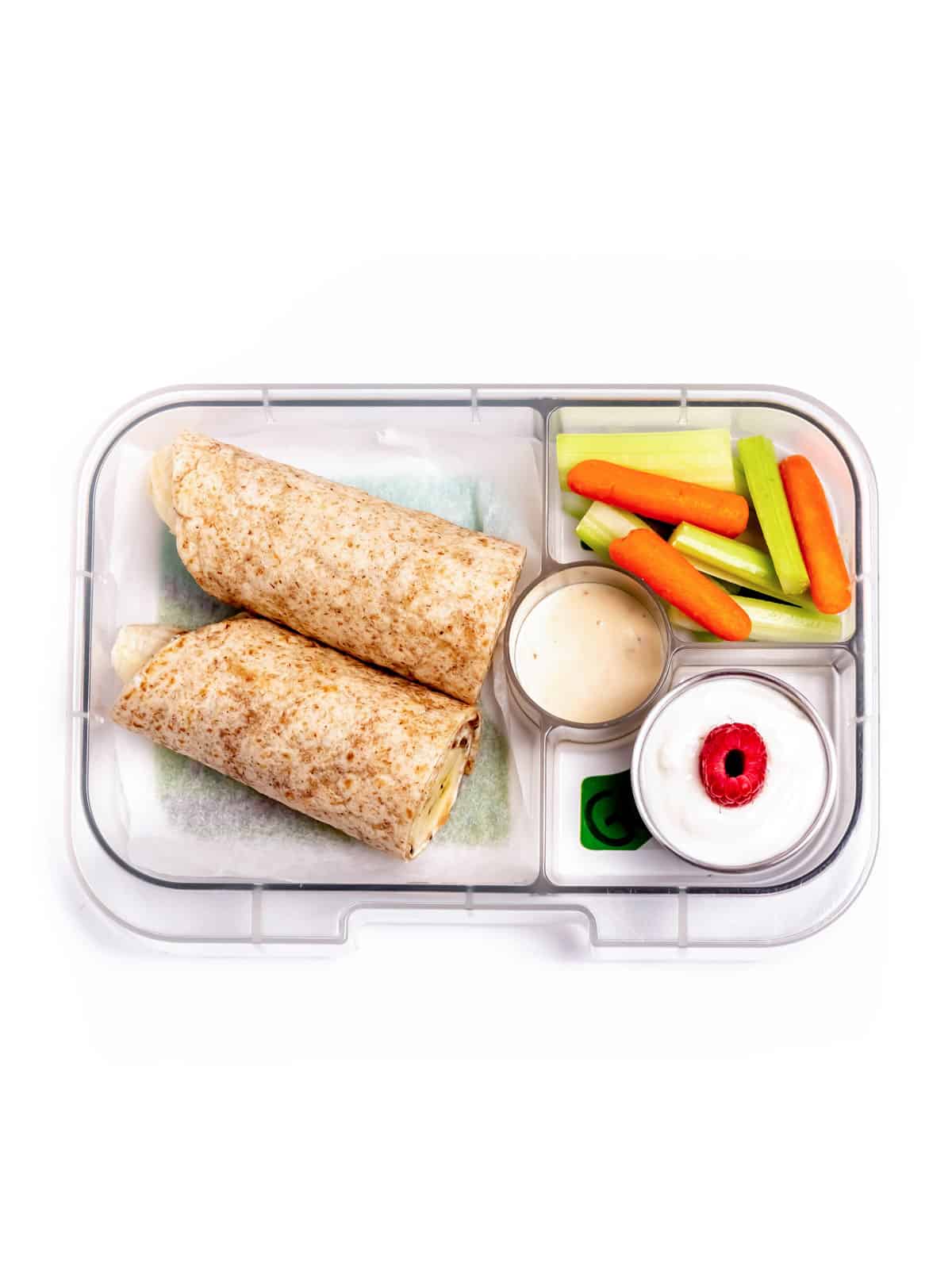 A lunch box with a banana and cream cheese wrap with yogurt, veggies and dip.