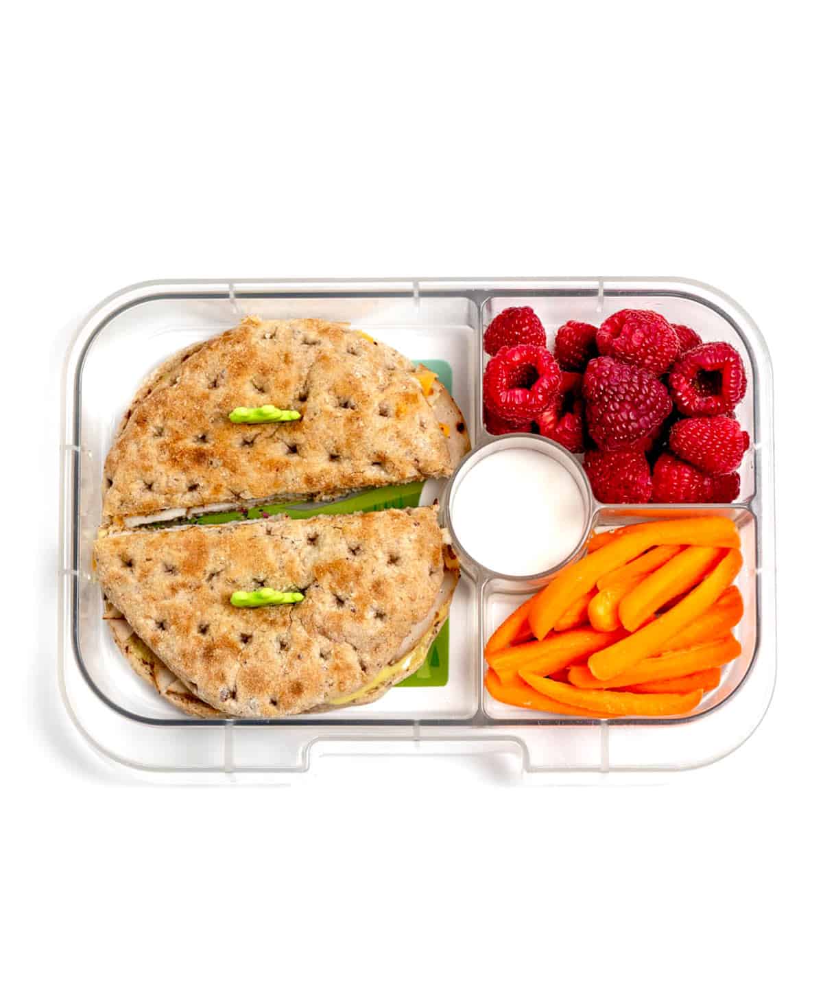 A turkey, cheese and honey mustard sandwich with carrot slices, dip and raspberries.
