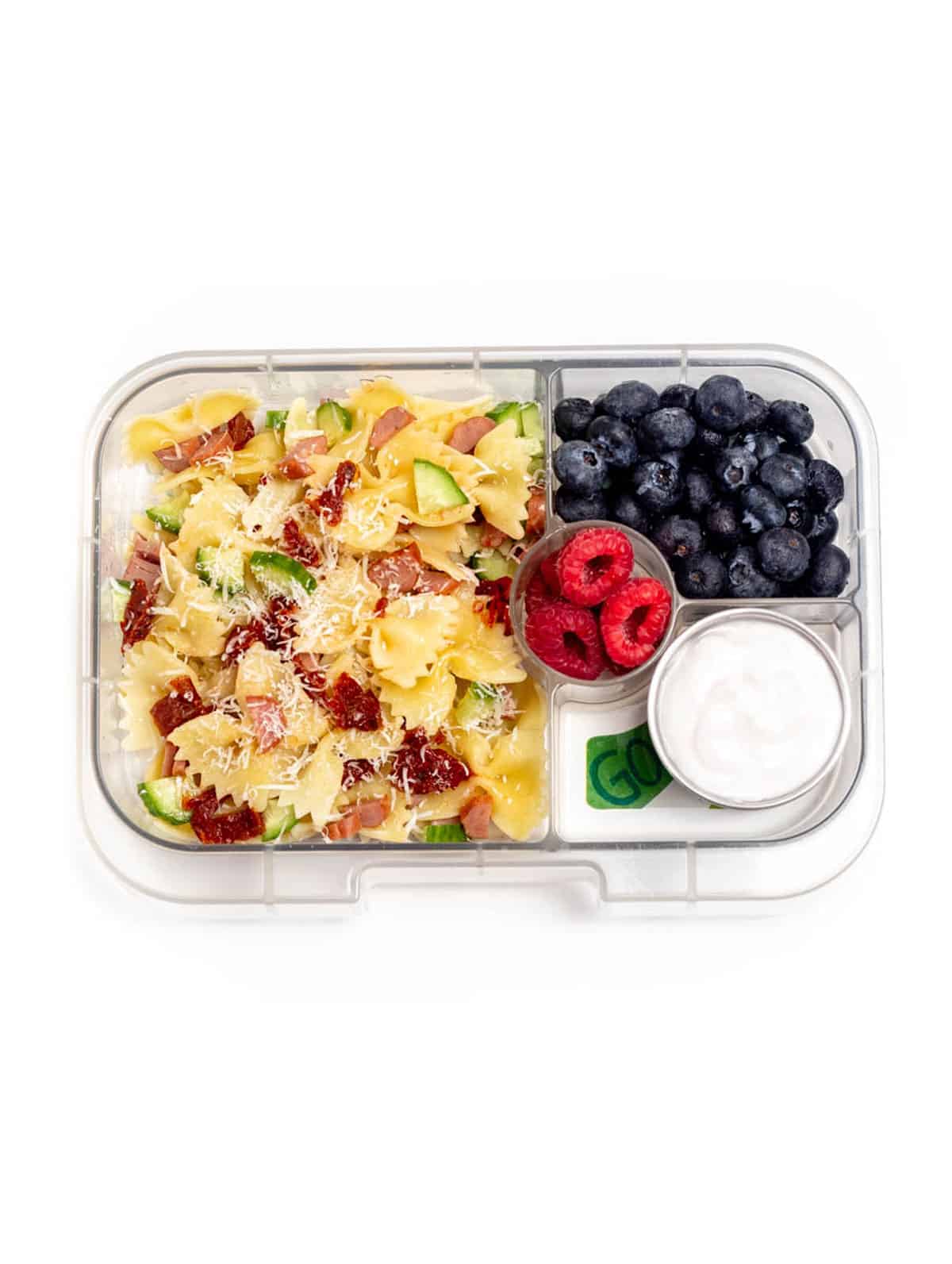 A lunch box with pasta salad, blueberries, raspberries and yogurt.