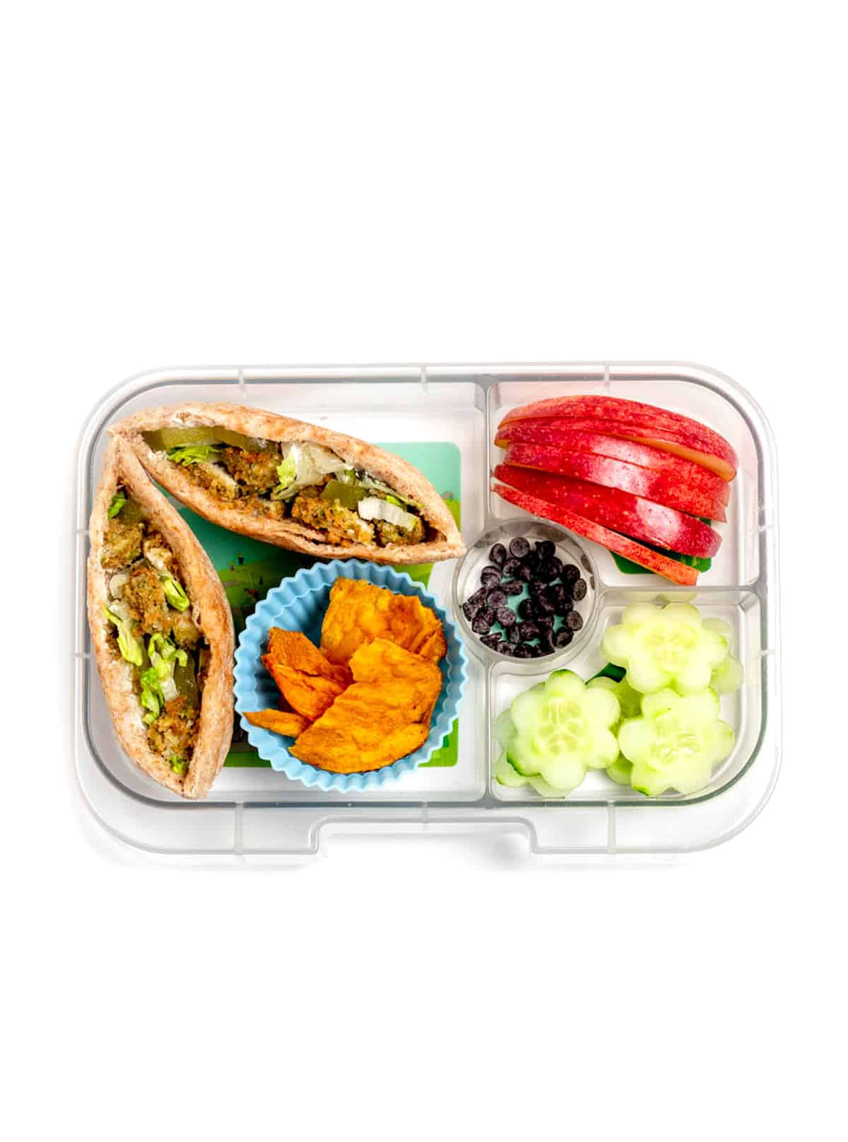 A lunch box with falafel pita with sweet potato chips, flower cucumbers, apple slices and mini chocolate chips.