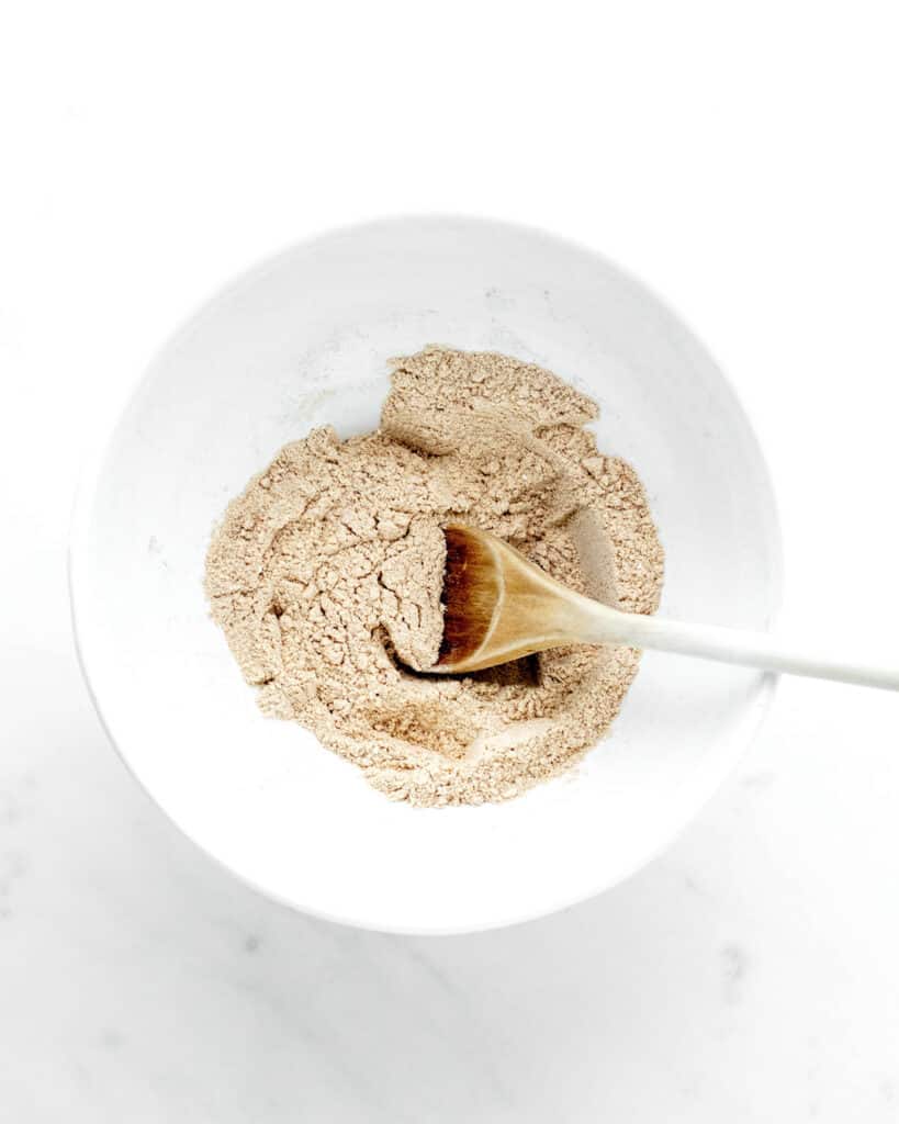 Dry ingredients for date muffins mixed together in a bowl with a wooden spoon.