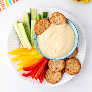 Two pita crackers being dipped into a bowl of hummus with Greek yogurt.