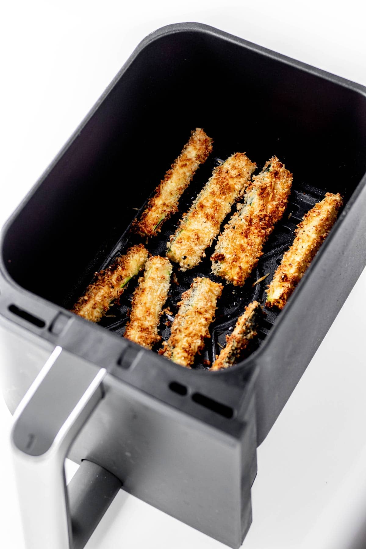 Close up image of zucchini fries in an air fryer basket.
