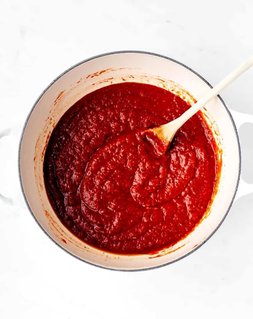 The cooked pizza sauce in a large pot with a wooden spoon.