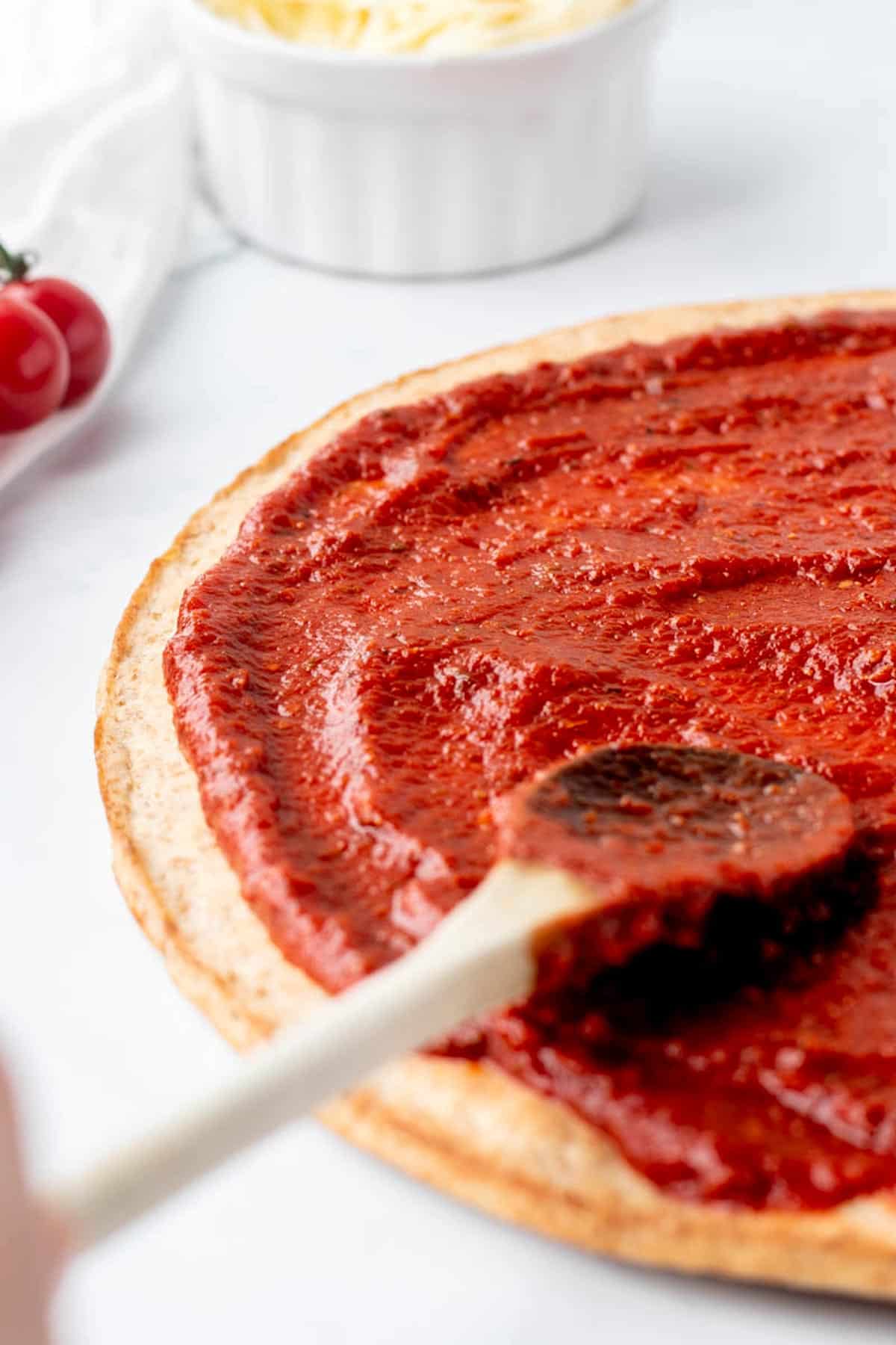Healthy pizza sauce being spread on pizza crust with a wooden spoon.