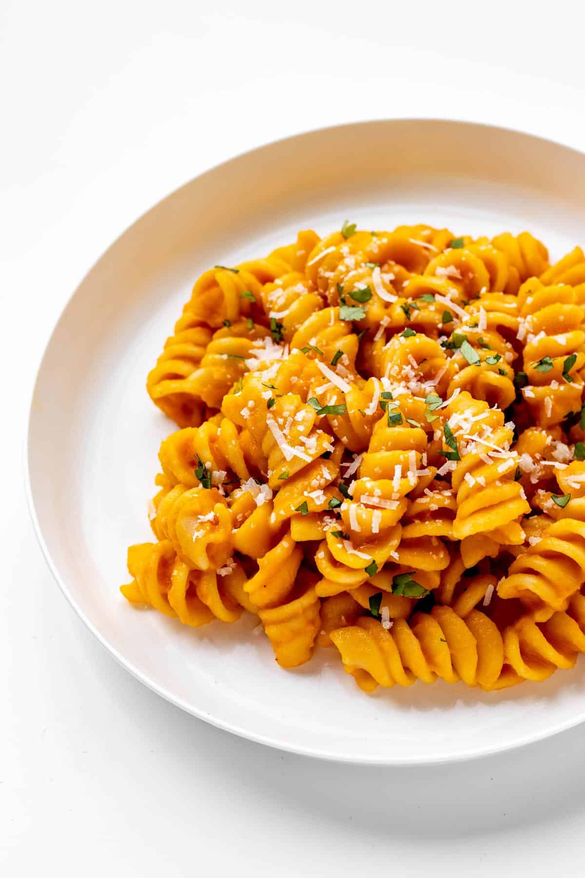 Roasted carrot pasta on a plate topped with a sprinkle of parmesan and chopped parsley.