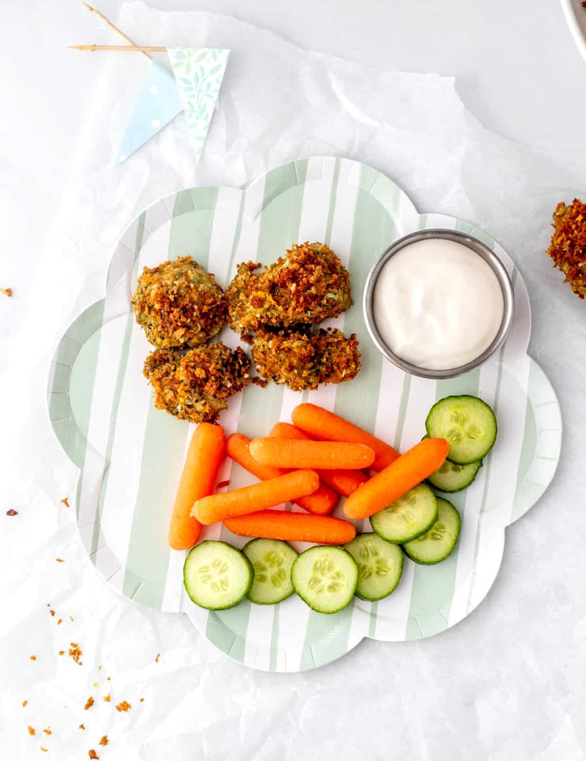 Four pesto chicken nuggets on a plate with raw veggies and dip.