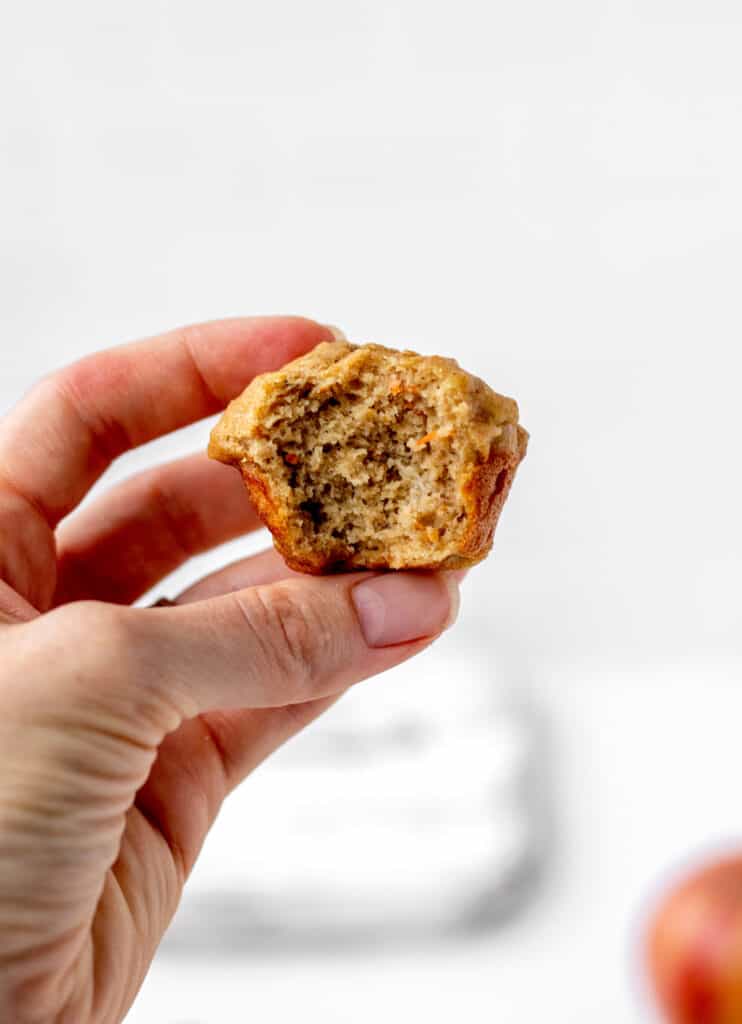 A hand holding up a mini abc muffin with a bite taken out of it.