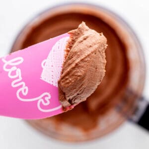 An up close image of chocolate frosting without powdered sugar on a pink spatula.