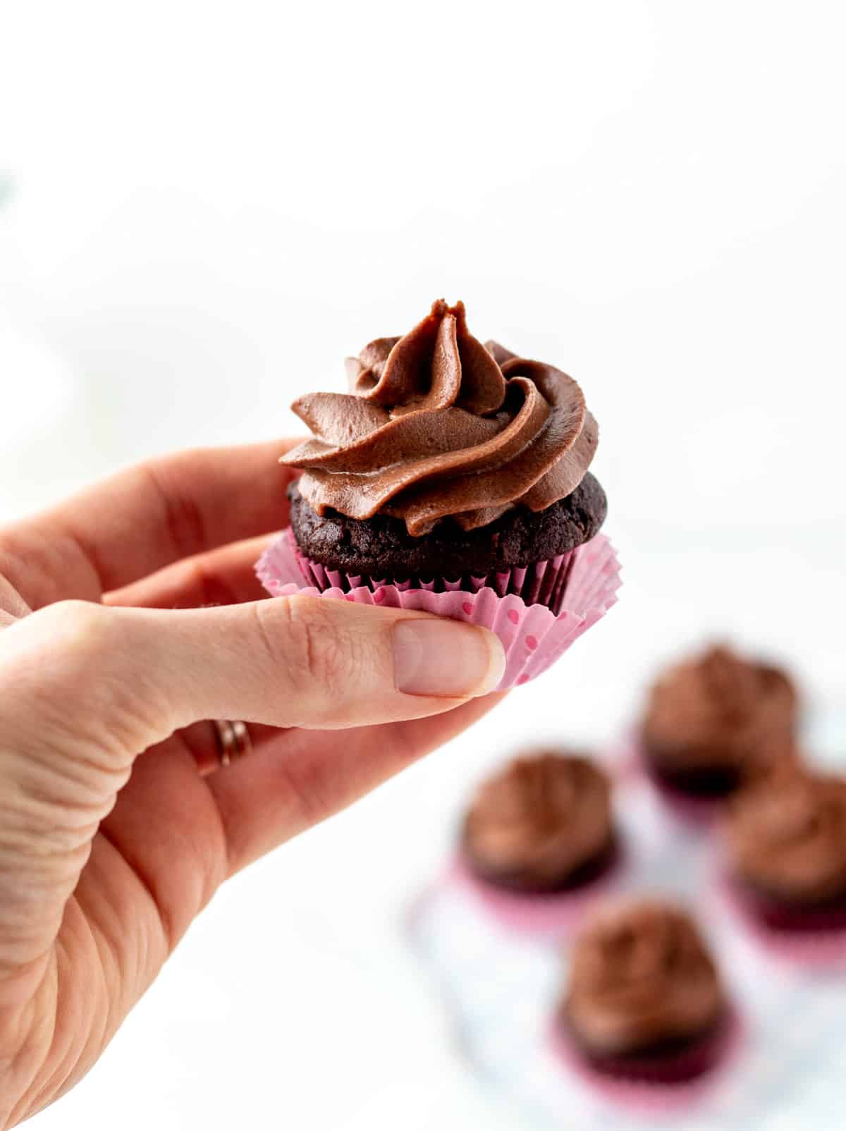 A hand holding up a mini cupcake with chocolate date frosting.