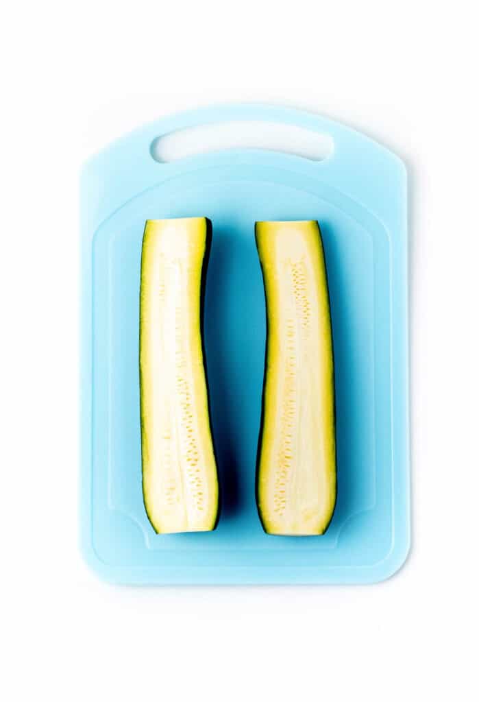 A zucchini cut in half on a blue cutting board.