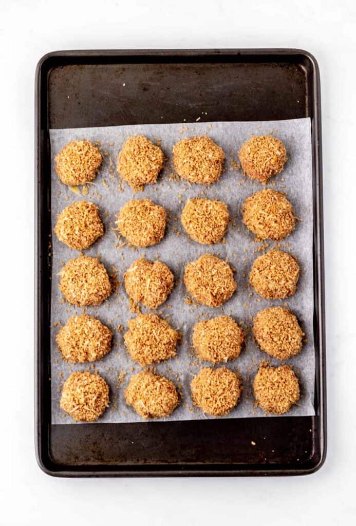 Ground chicken nuggets dipped in the breadcrumbs coating on a baking sheet.