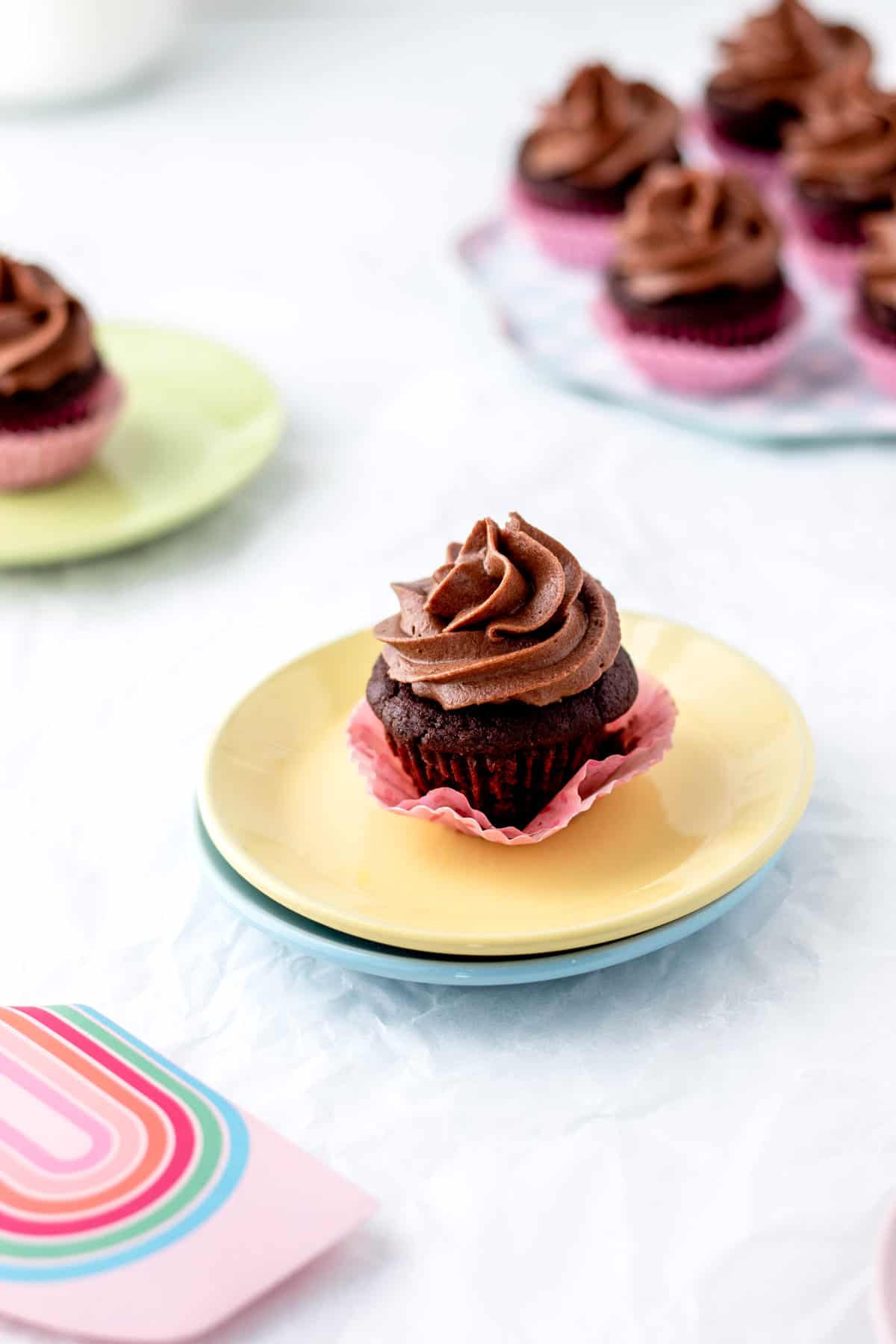 A frosted mini chocolate cupcake on two colourful stacked plates.