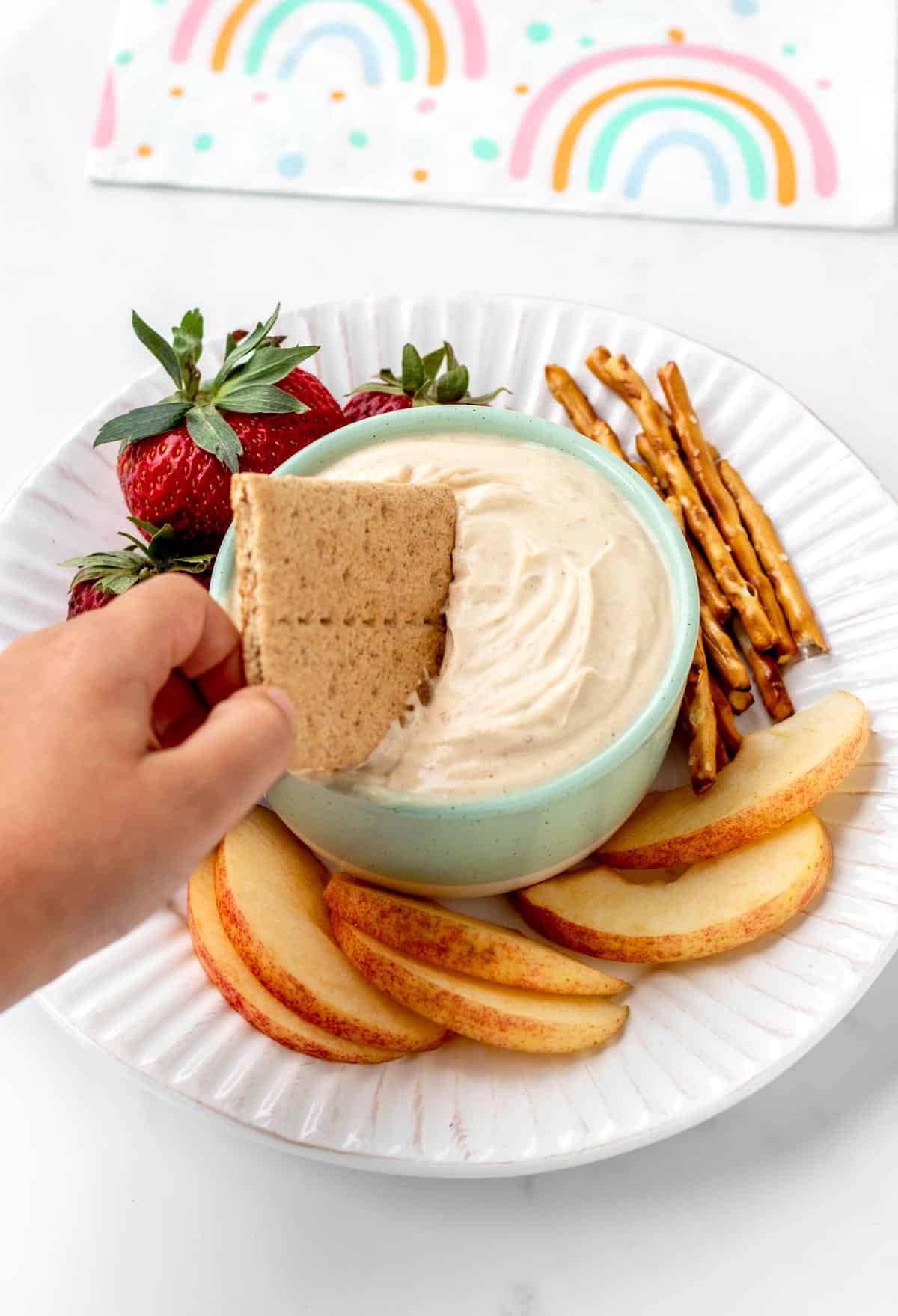 A child's hand dipping a graham cracker into a bowl of 4-ingredient peanut butter dip.