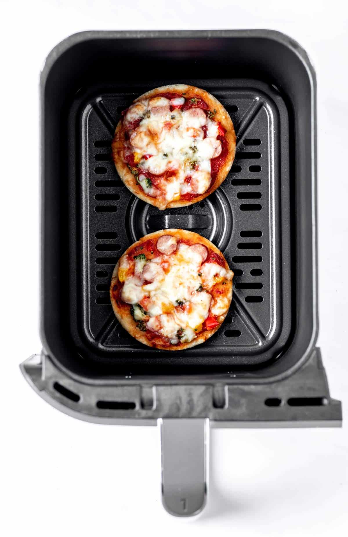 Cooked healthy mini pizzas in air fryer basket.