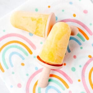 Up close image of two mango popsicles for toddlers on a rainbow napkin.