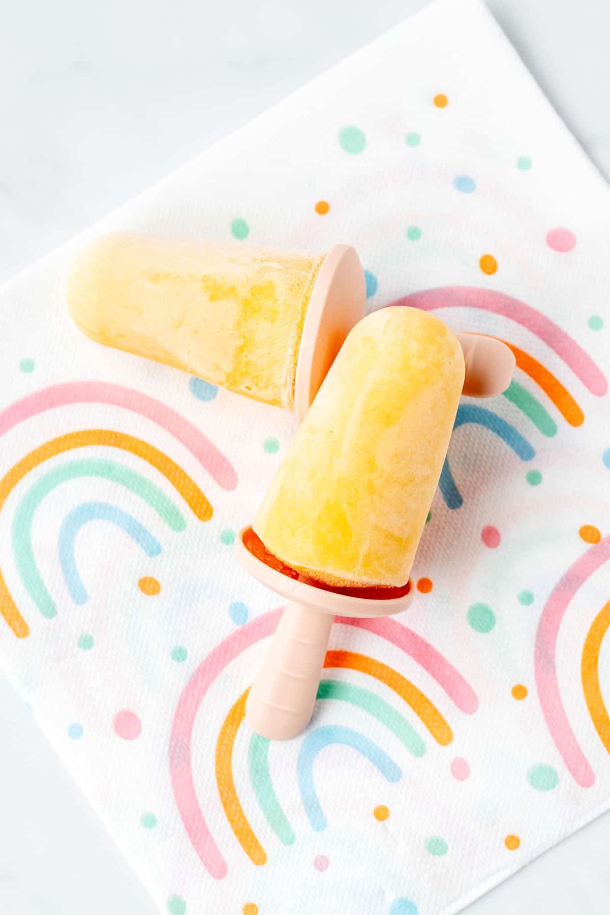 Two mango popsicles for toddlers on a rainbow napkin.