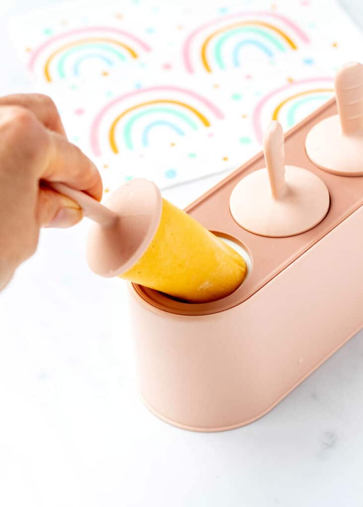 A hand removing a mango popsicle for a popsicle mold.