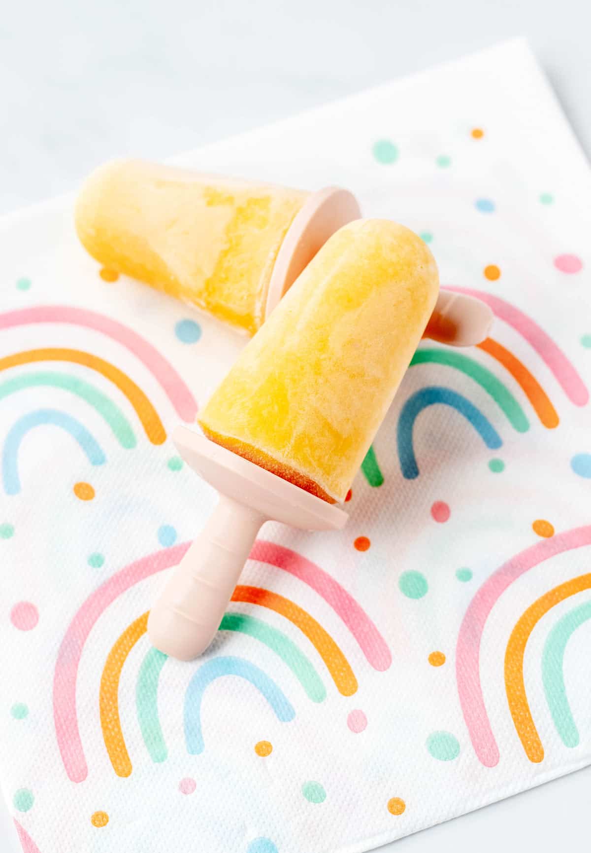 Two mango popsicles for toddlers on a rainbow napkin.