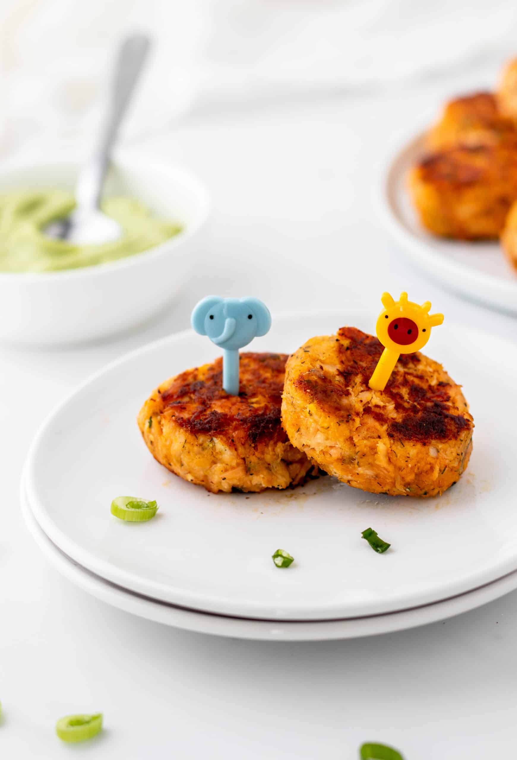 Two mini salmon cakes on a small plate with cute little picks.