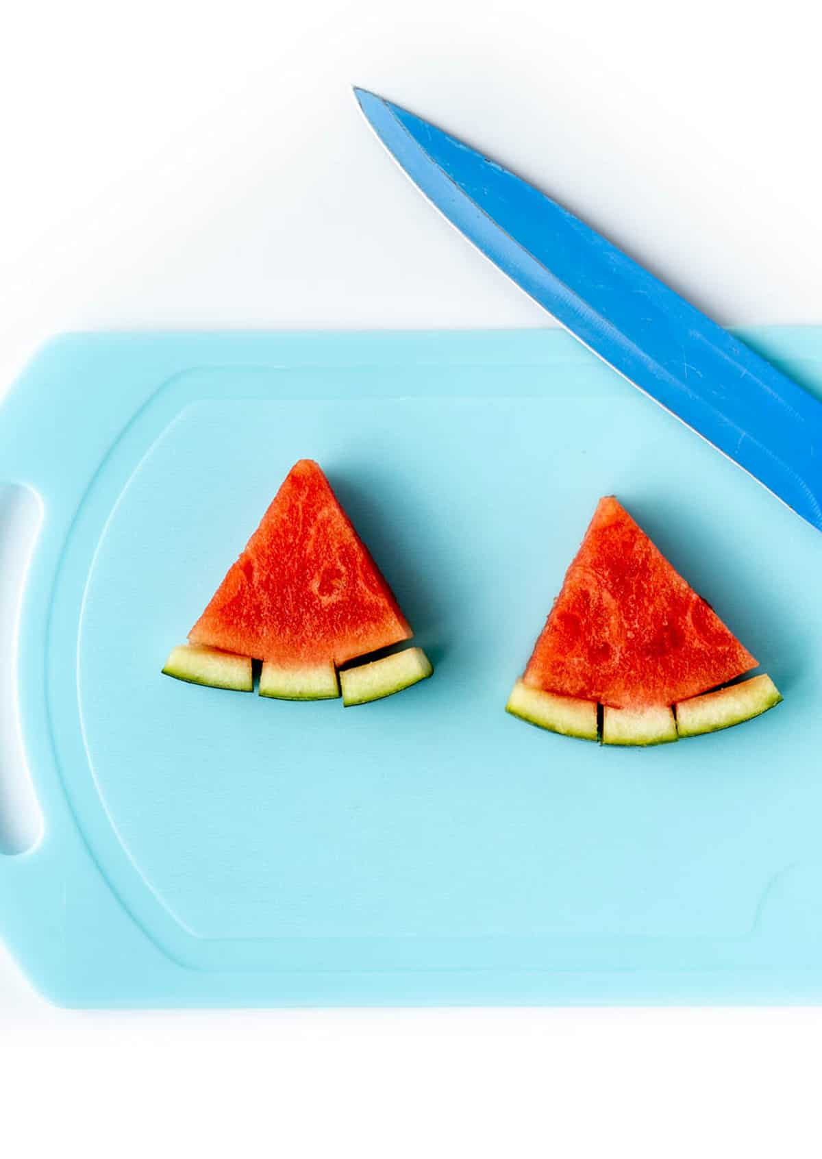 Two watermelon Christmas trees on a blue cutting board with a knife.
