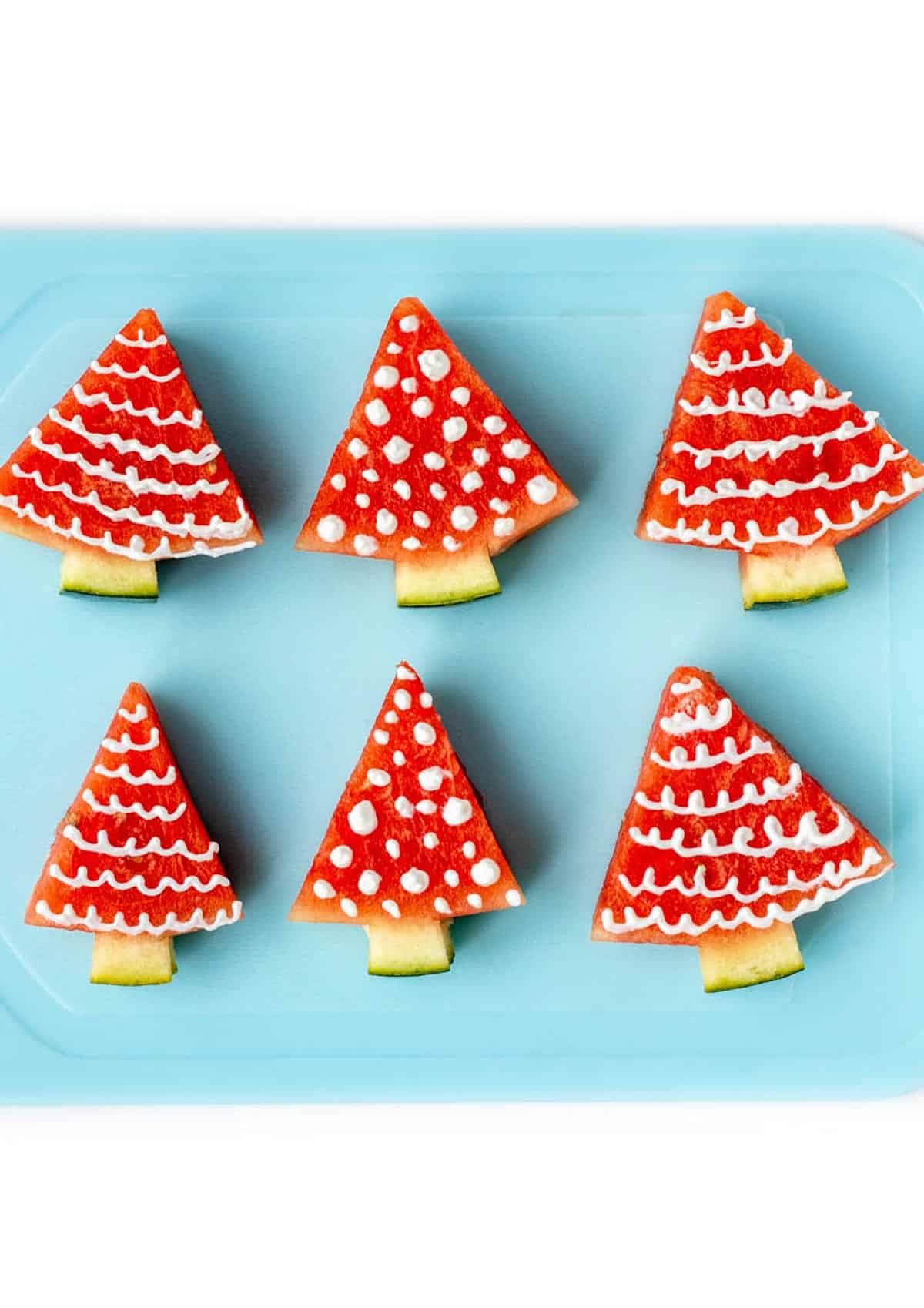Decorated watermelon Christmas trees on a blue cutting board.
