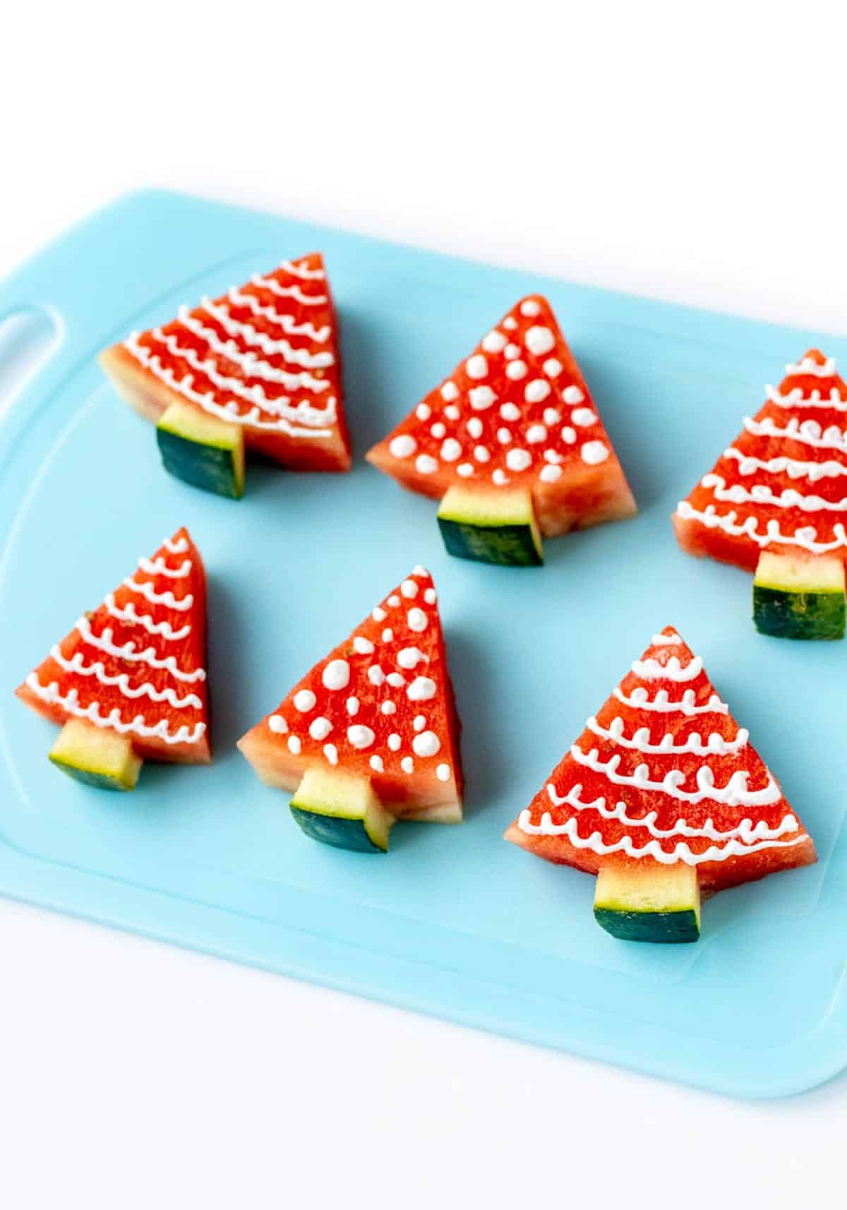 Watermelon Christmas trees decorated with yogurt on a cutting board.