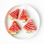 Four watermelon Christmas trees with yogurt decorations on a white plate.