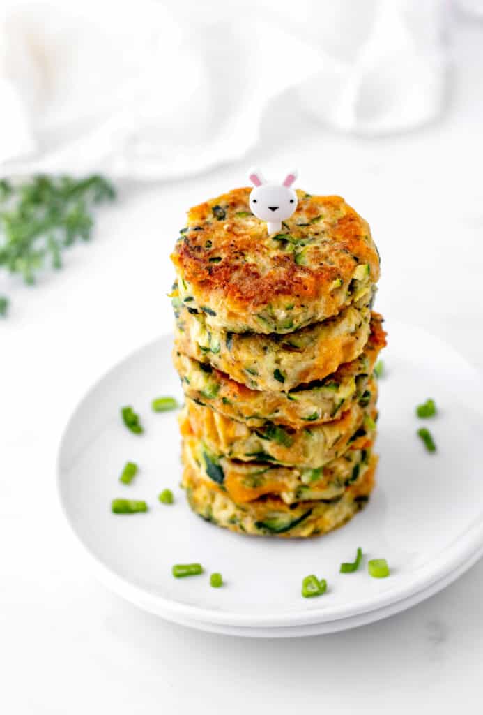A stack of cheesy zucchini fritters on a white plate with a bunny pick.